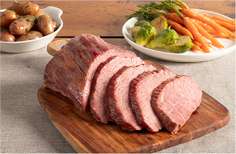 sliced Grobbel's corned beef, with a plate of carrots and brussels sprouts in the background